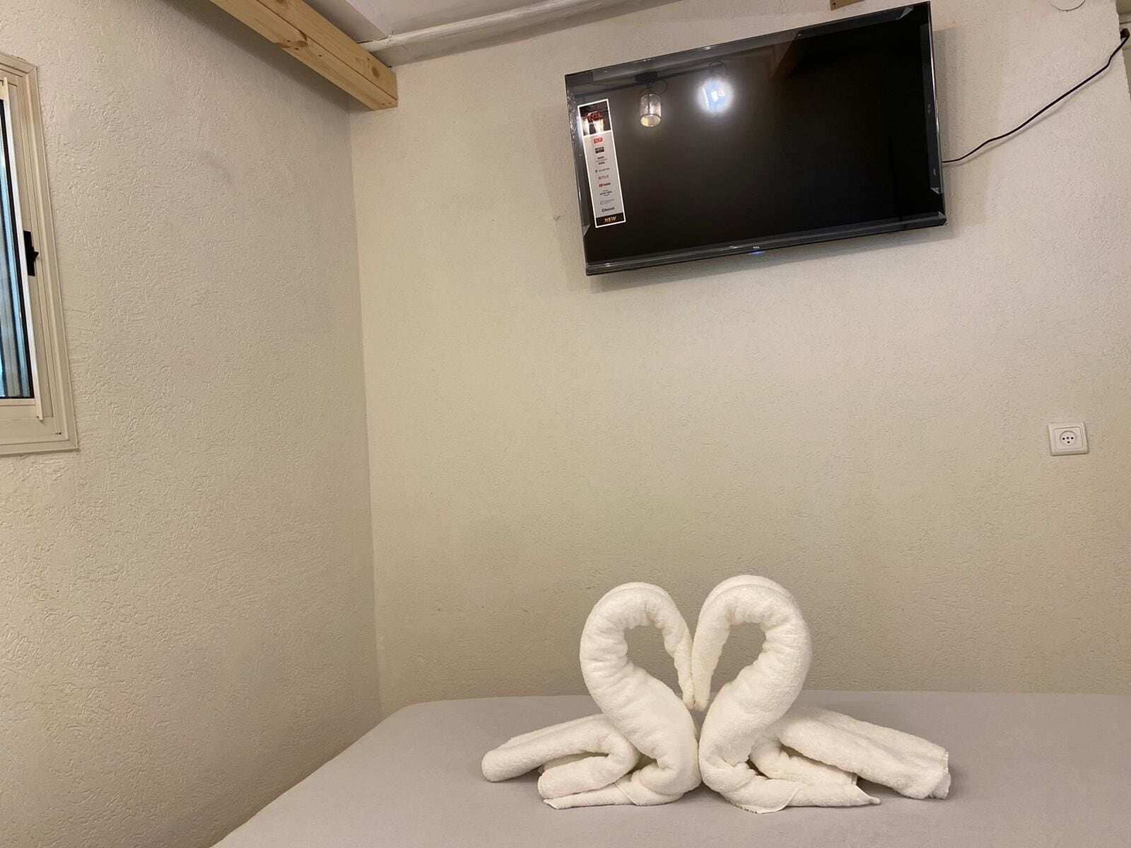 A room with a bed, a flat-screen TV mounted on the wall, and a power outlet.