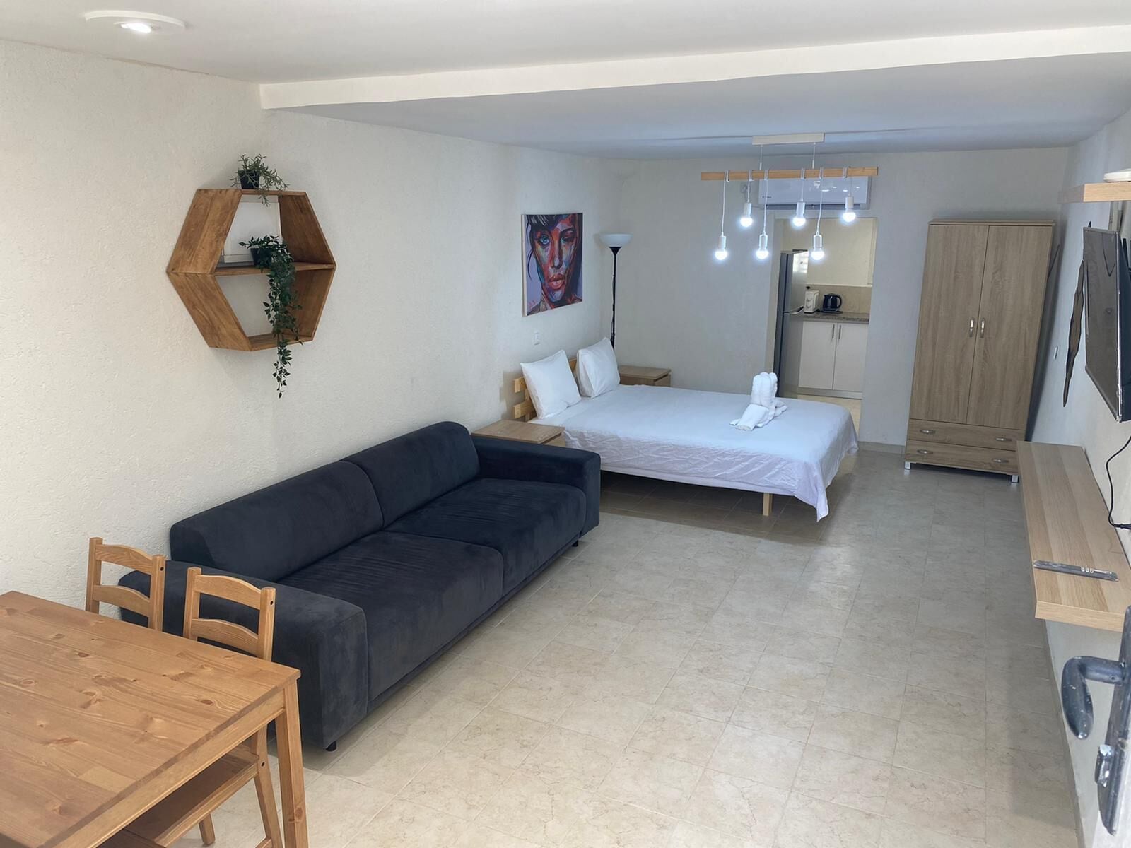 A modern, well-lit room with a sofa, a bed, a wooden dining table, and a cabinet.