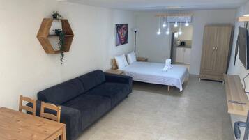 A modern, well-lit room with a sofa, a bed, a wooden dining table, and a cabinet.