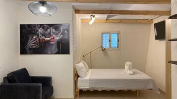 A compact bedroom with a bed, a black chair, a painting, a window, and a ceiling light.