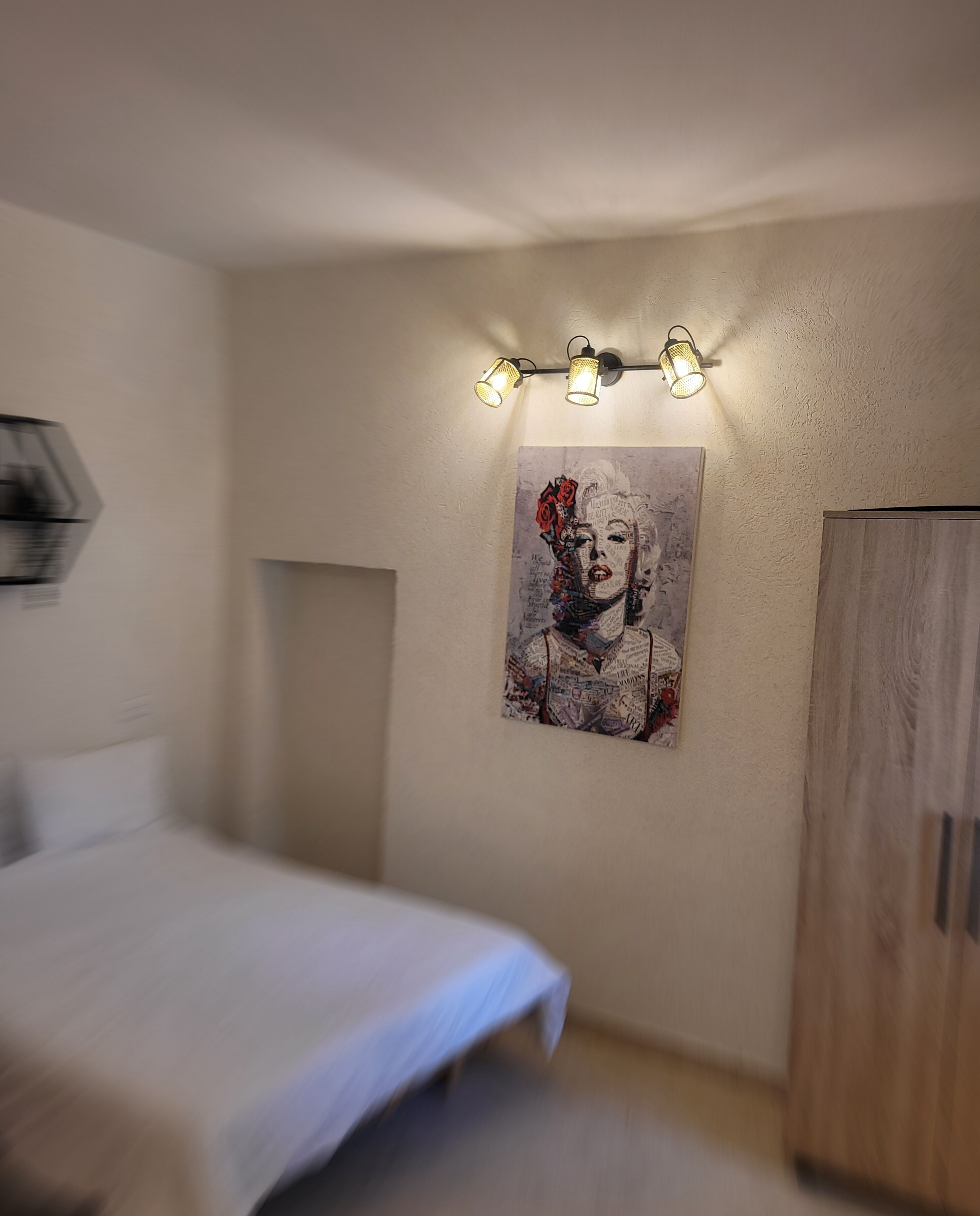 A bedroom with a bed, a wardrobe, and a wall-mounted light fixture.