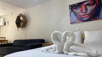 Une chambre d’hôtel avec un lit, un tableau au mur, une étagère en bois avec une plante et un canapé noir.