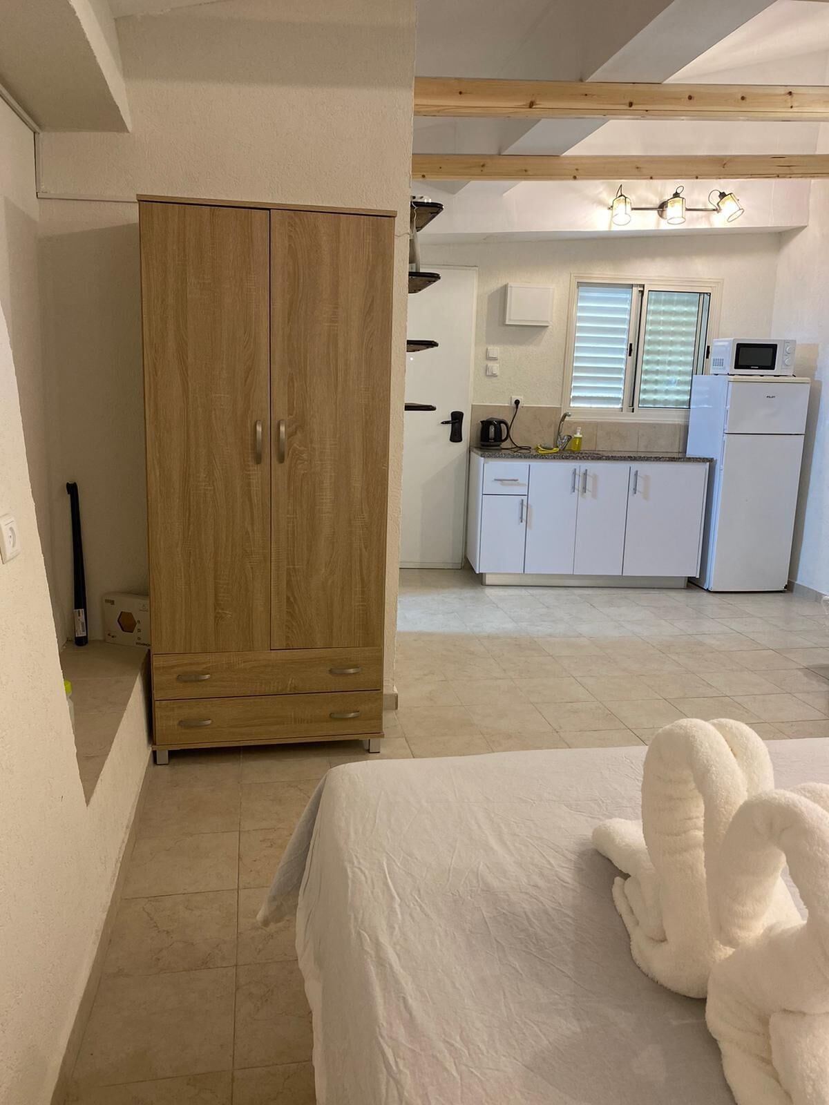 Quarto com cama grande, guarda-roupa de madeira e cozinha compacta equipada com micro-ondas e frigorífico.