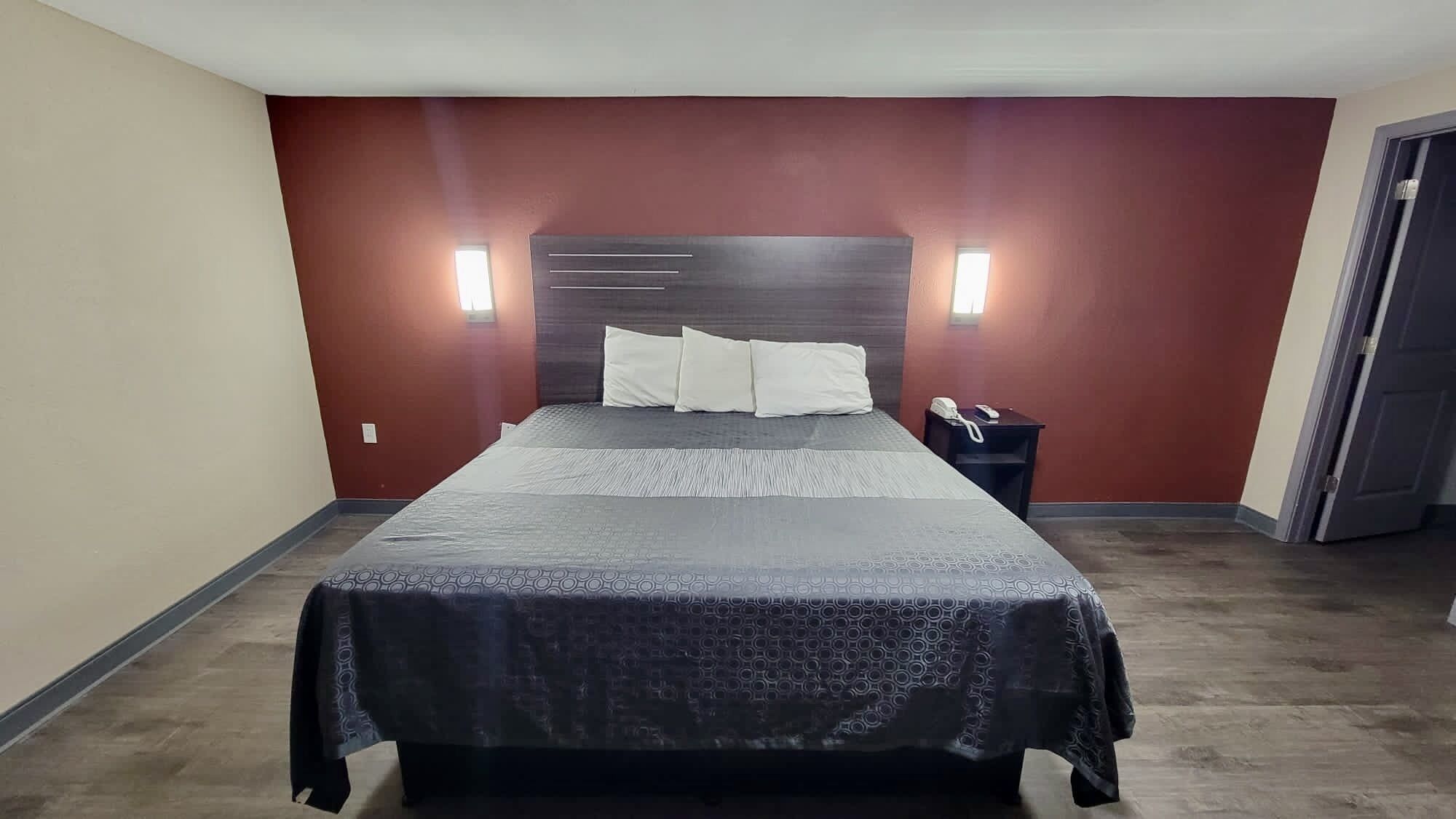 A hotel room with a large bed, two bedside tables, and a red accent wall.