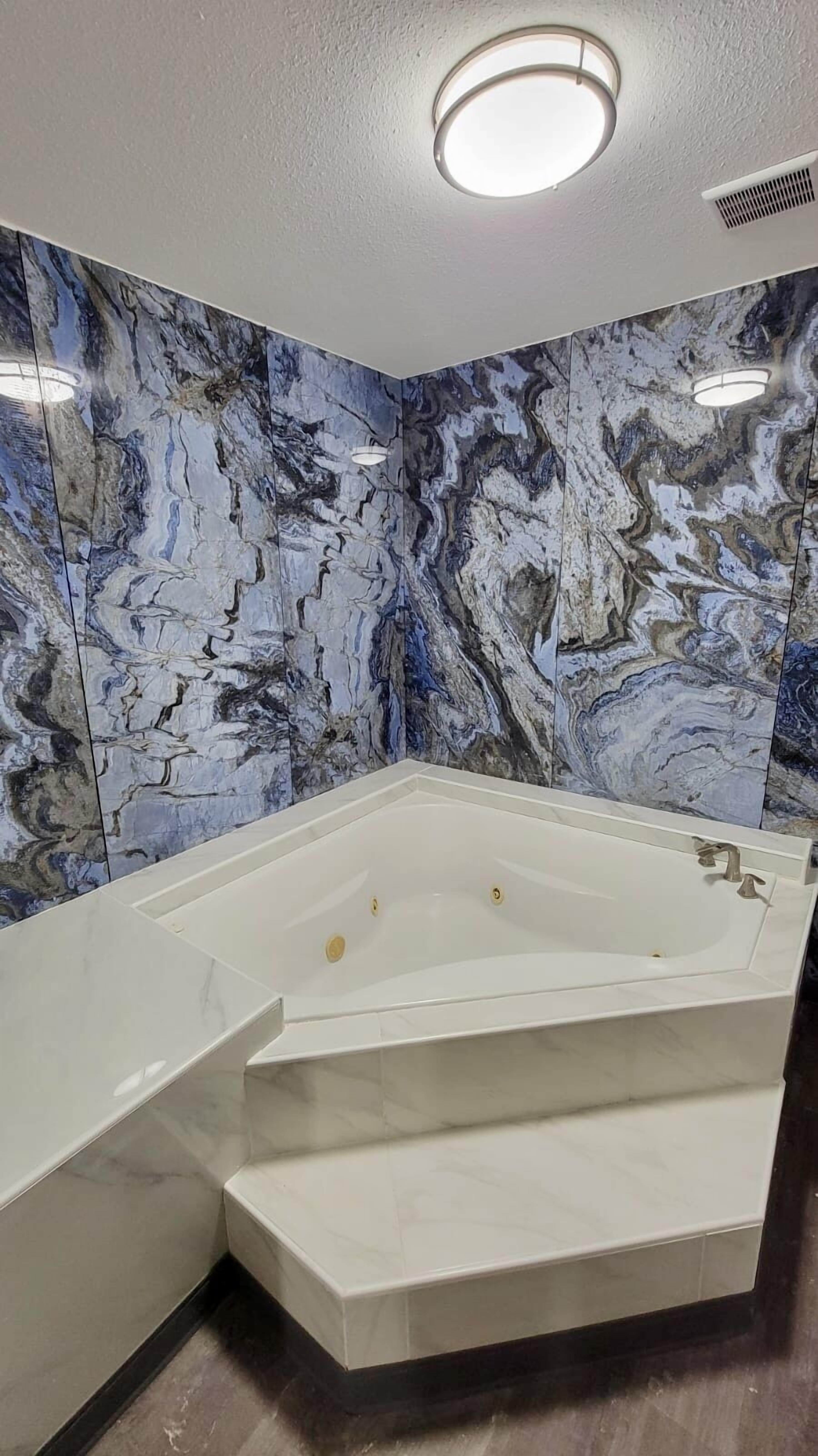 A bathroom with a marble wall, a bathtub, and a shower area.