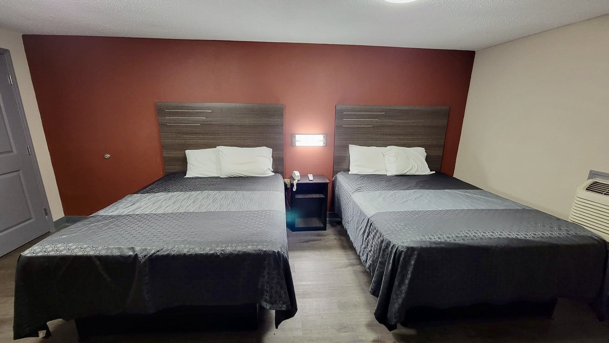 A hotel room with two single beds, a nightstand with a phone, and a wall-mounted light.