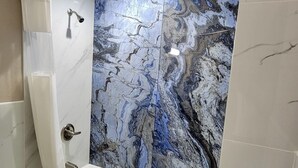 Un baño moderno con pared de mármol, una bañera y zona de ducha.