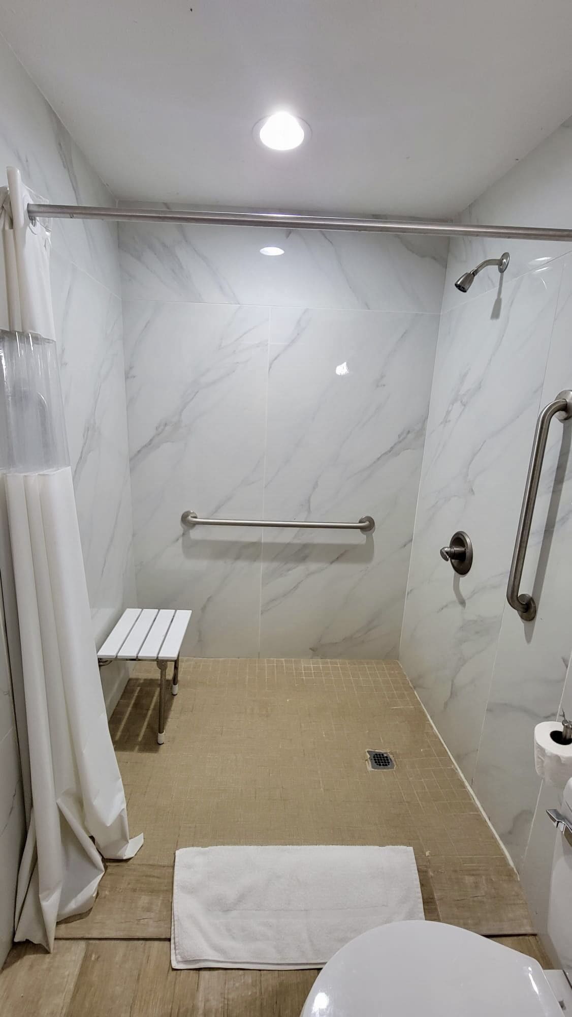 A modern bathroom with a walk-in shower, a bench, a grab bar, and a toilet.