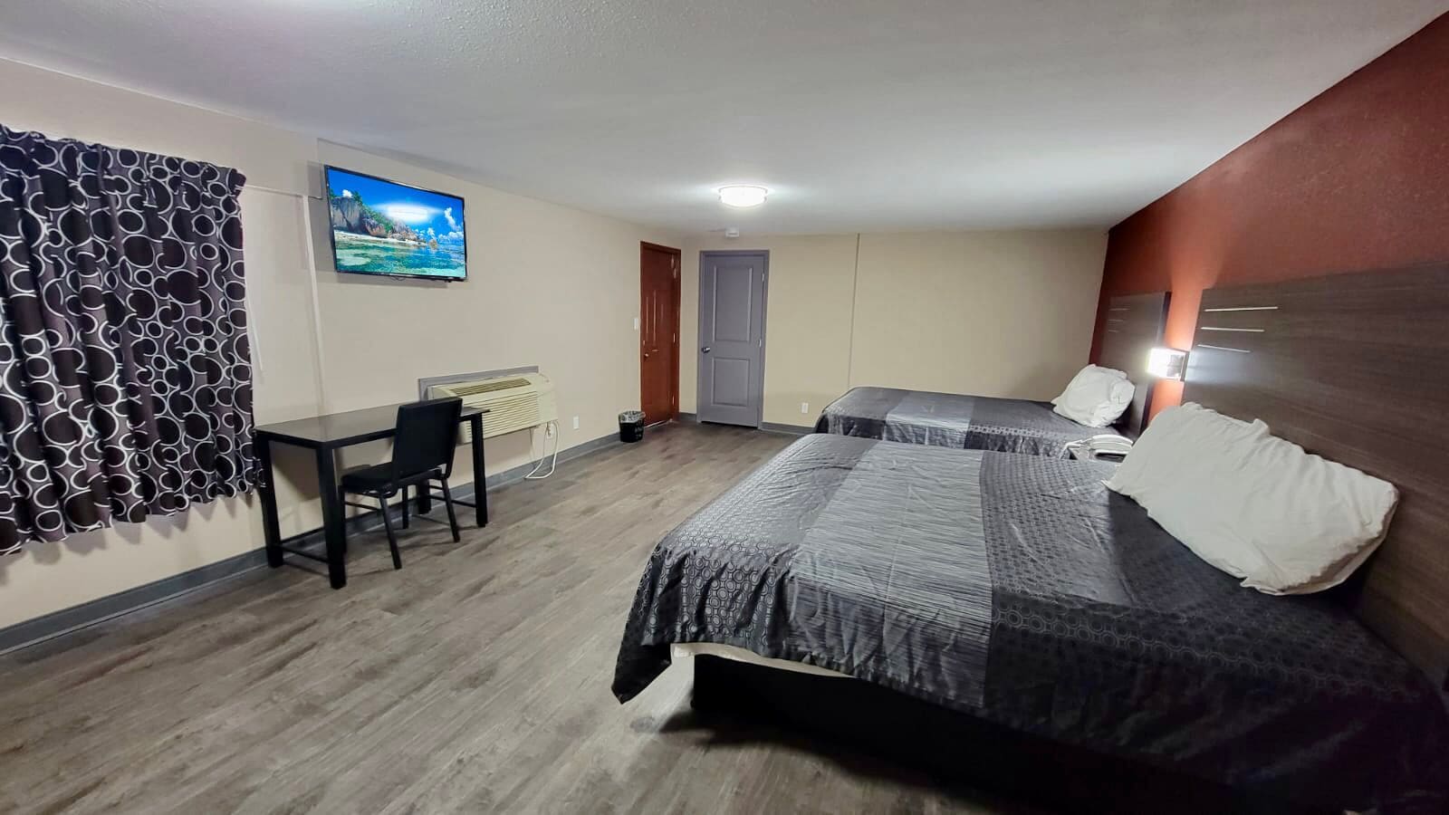 A hotel room with two beds, a desk, a chair, a TV on the wall, and a door.