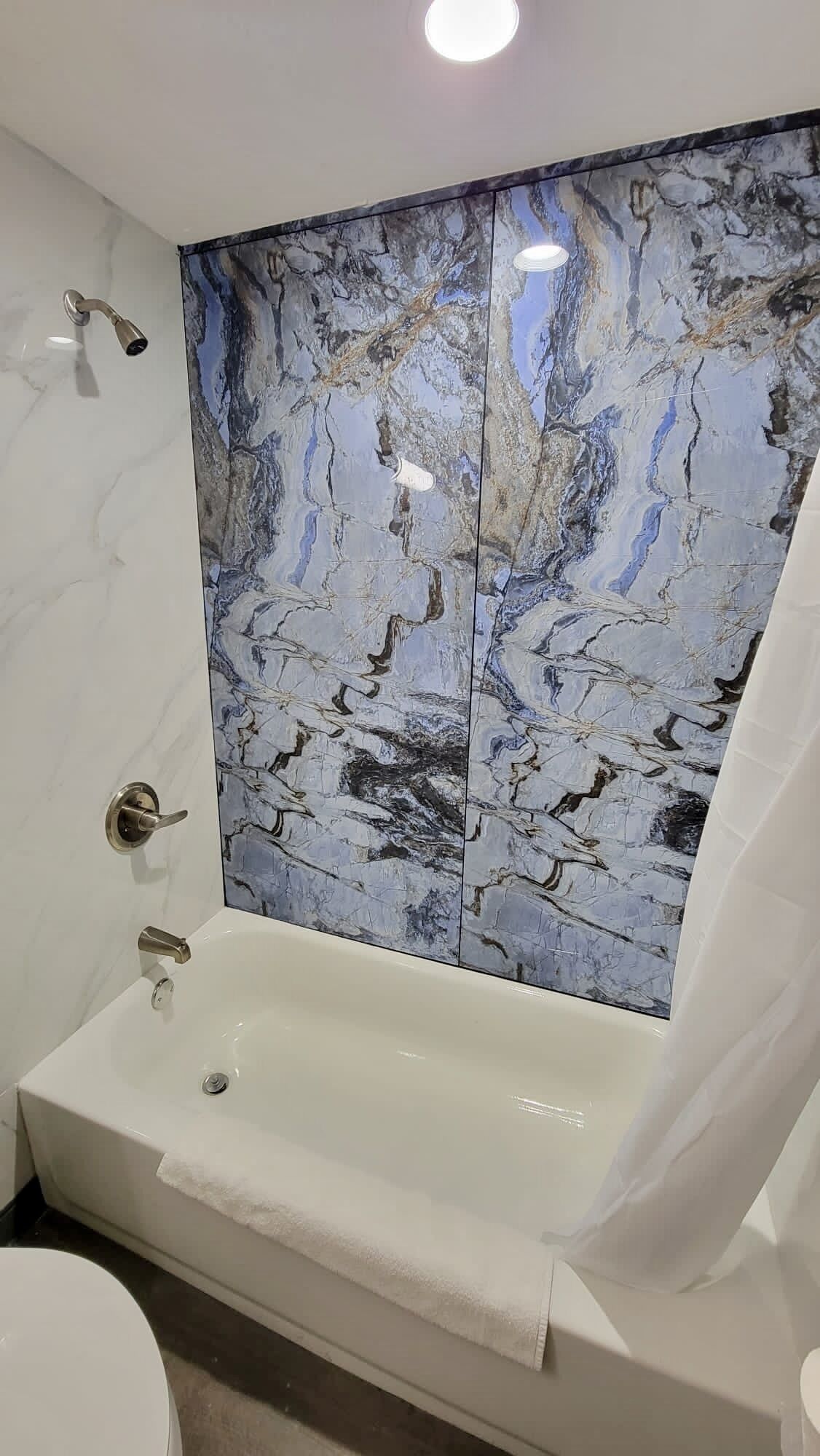 A bathroom with a marble shower wall, a bathtub, and a toilet.