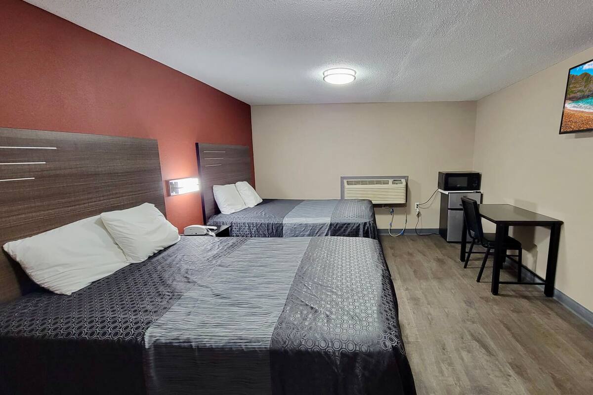Habitación de hotel con dos camas, un escritorio, un televisor y un cuadro de un paisaje natural.