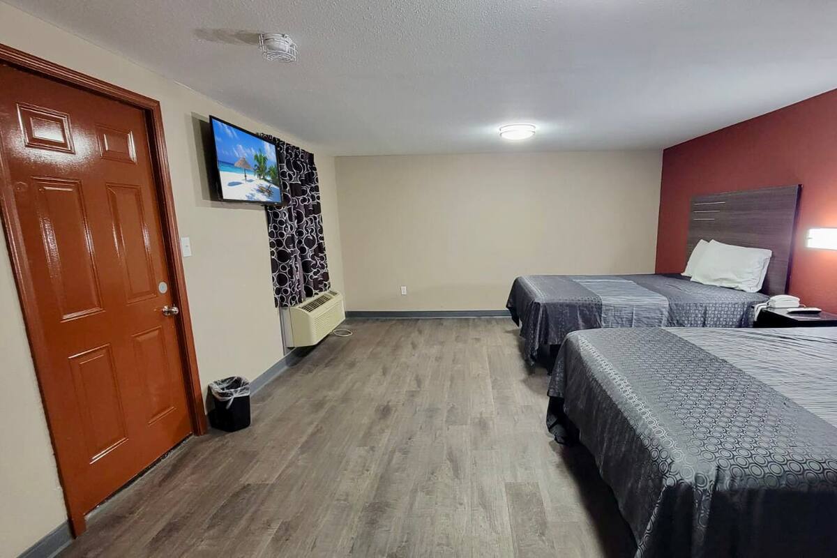 Una habitación de hotel con dos camas, televisión, calentador en la pared y una puerta.