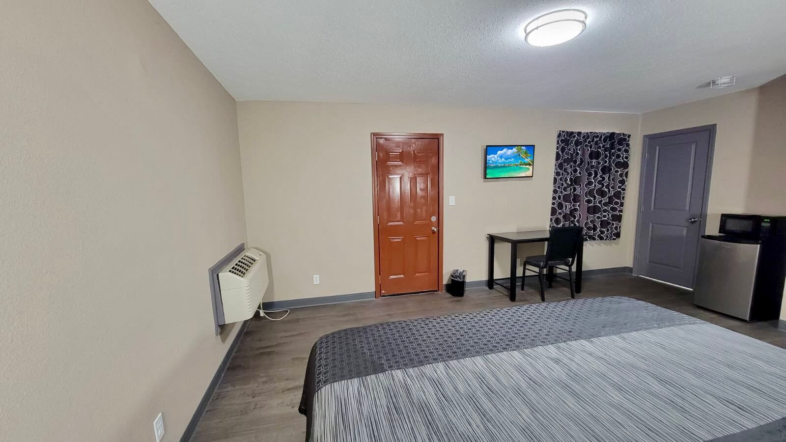 Ein Hotelzimmer mit Bett, Schreibtisch, Stuhl, Kühlschrank und einer Tür.