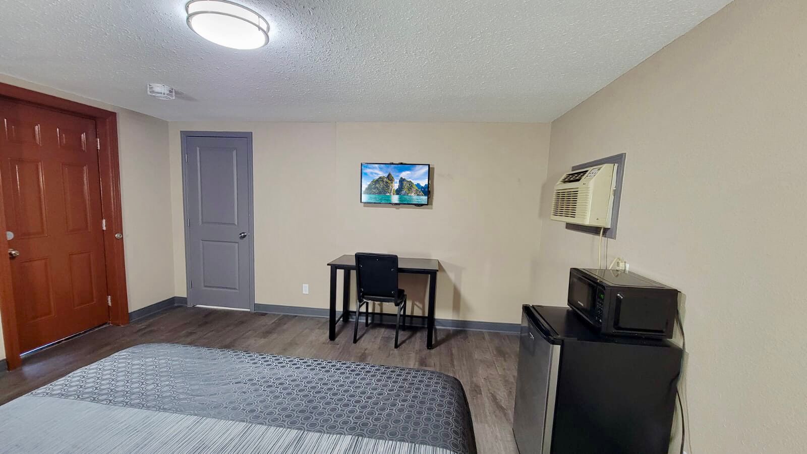 Una habitación de hotel con cama, escritorio con silla, televisor y aire acondicionado.