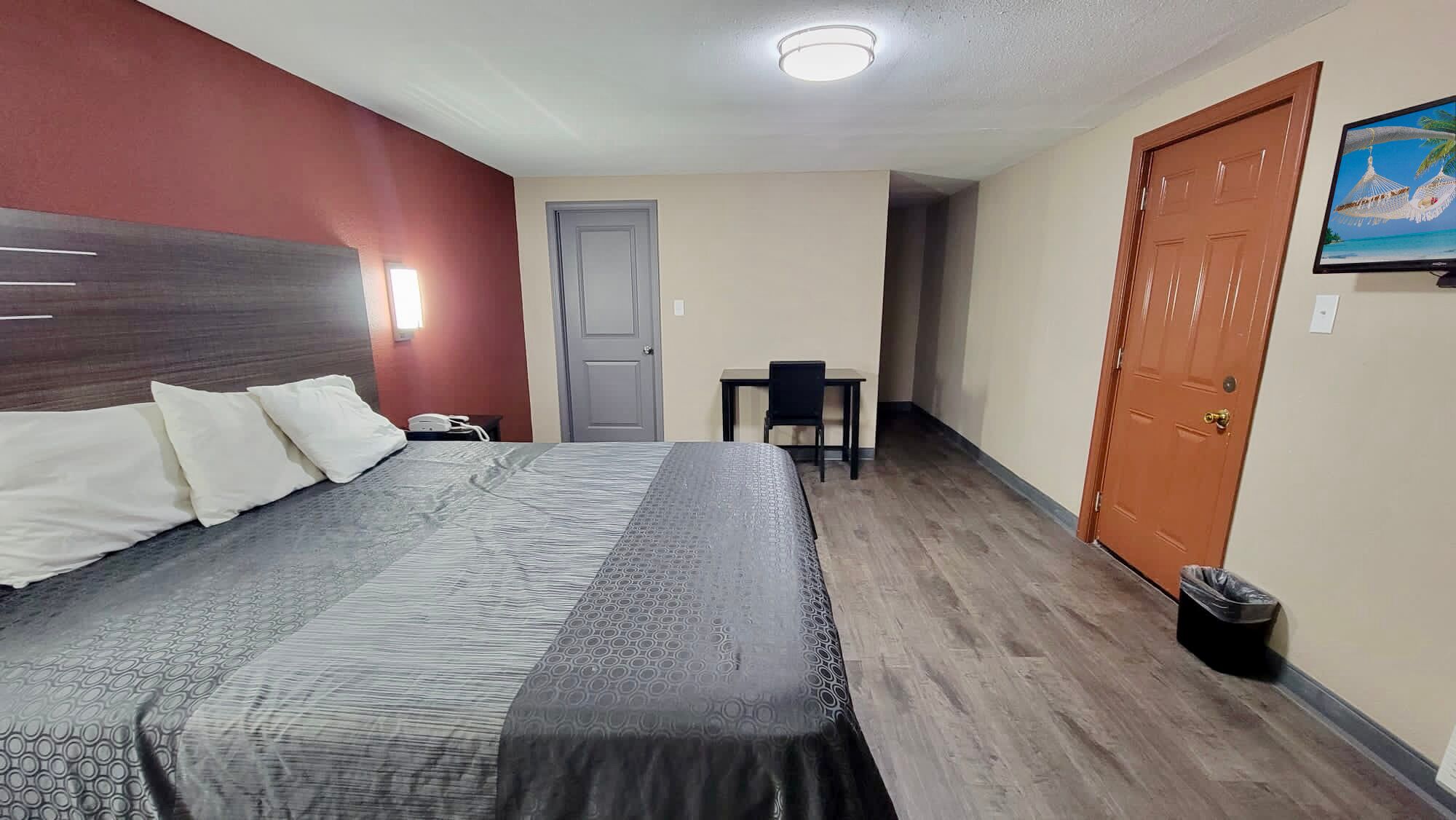 Habitación de hotel con cama, escritorio, silla, televisor y puerta.