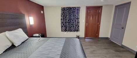 Une chambre d’hôtel avec un lit, un téléphone, une porte et un rideau.