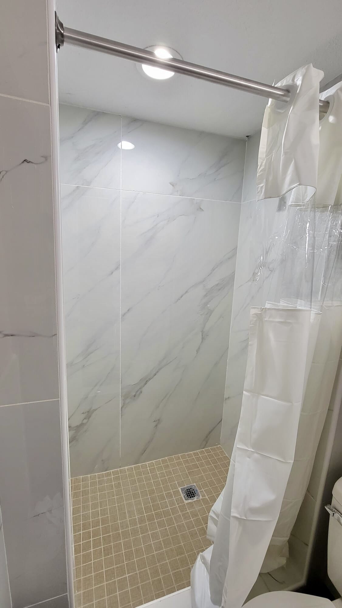 A shower area with a glass door, marble walls, and a tiled floor.
