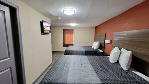 Habitación de hotel con dos camas, un televisor montado en la pared y una ventana con persianas.
