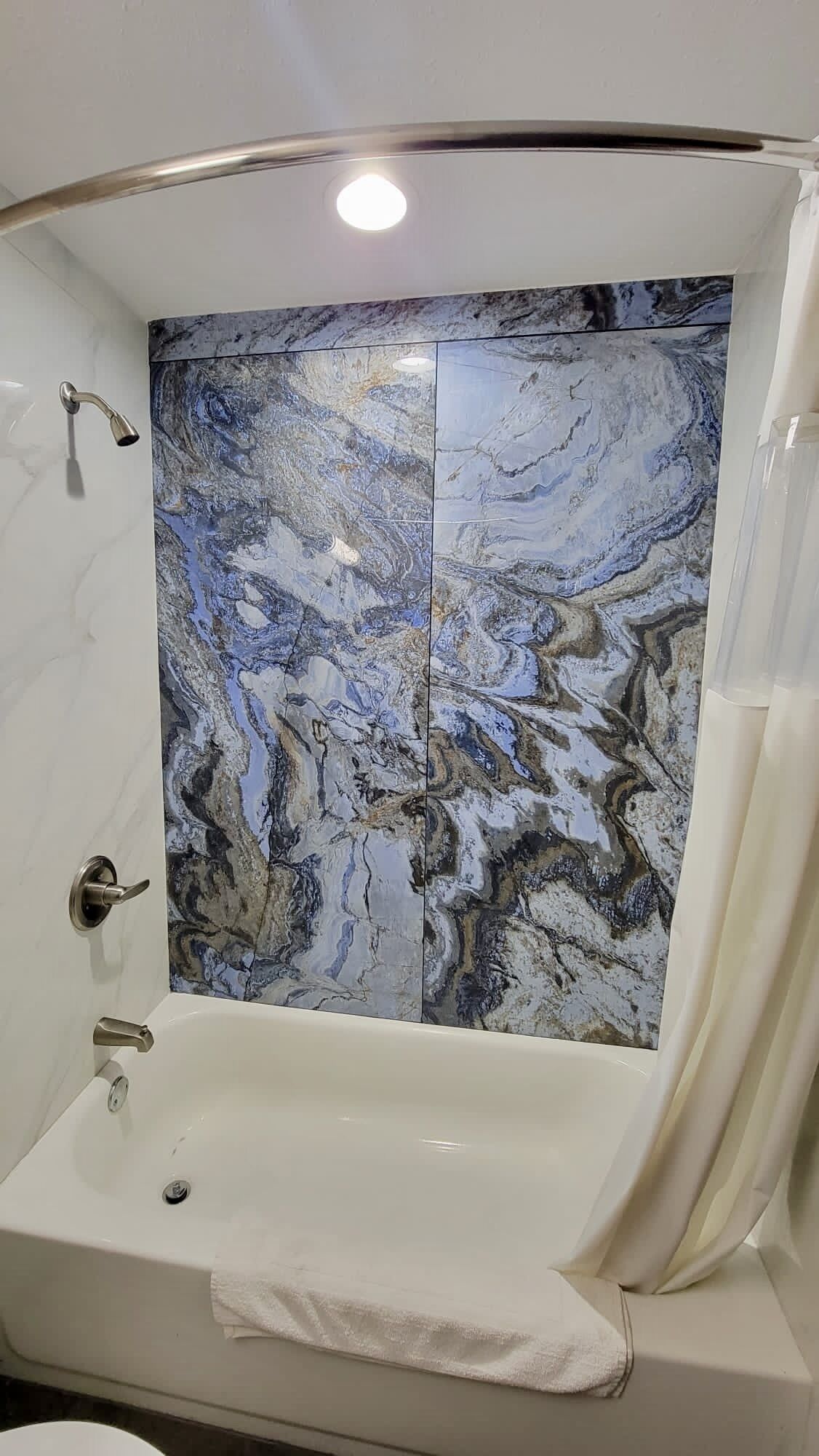 Un baño con pared de ducha de mármol, una bañera y un inodoro.