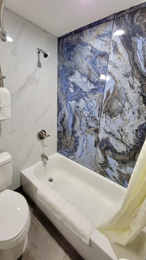A bathroom with a marble wall, a bathtub, and a toilet.