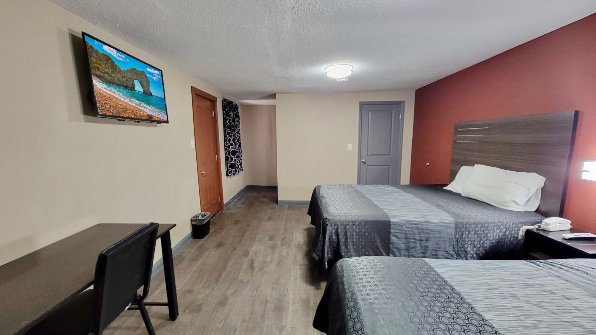 A hotel room with two beds, a desk, a chair, a TV on the wall, and a door.