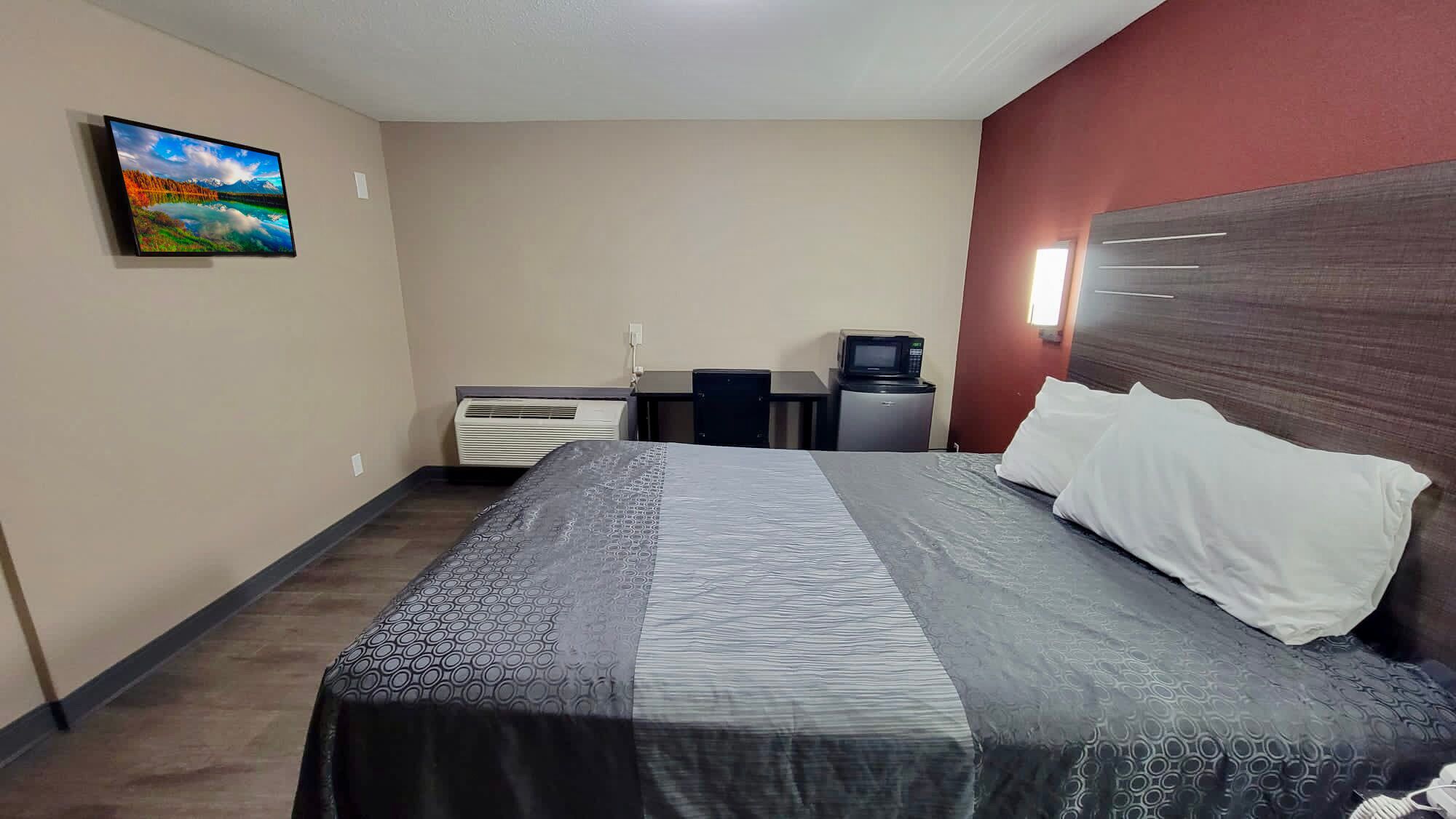 A hotel room with a bed, a desk, a chair, a microwave, and a television on the wall.