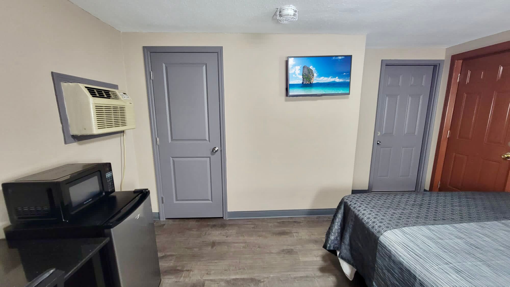 A hotel room with a bed, a desk with a computer, an air conditioner, and two doors.