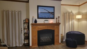 A living room with a fireplace, a television mounted above it, and a large window with curtains. - Beautiful Lake front property on Big Stone Lake (Clinton)