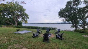 A grassy outdoor area with four Adirondack chairs facing a lake, a grill, and a picnic table. - Beautiful Lake front property on Big Stone Lake (Clinton)