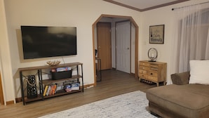A living room with a flat-screen TV, wooden furniture, a coffee-themed sign, and a door leading to another room. - Beautiful Lake front property on Big Stone Lake (Clinton)