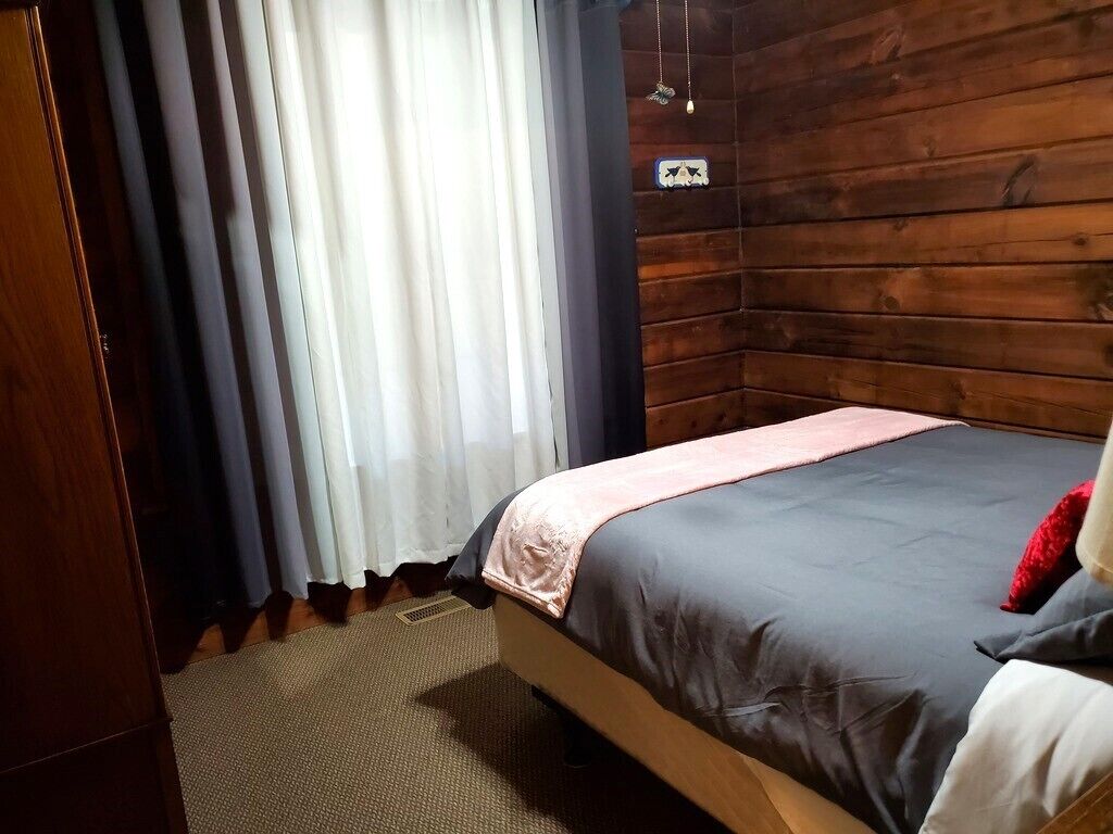Une pièce aménagée comme un chalet en bois, avec un lit, des rideaux et un petit panneau accroché au mur.