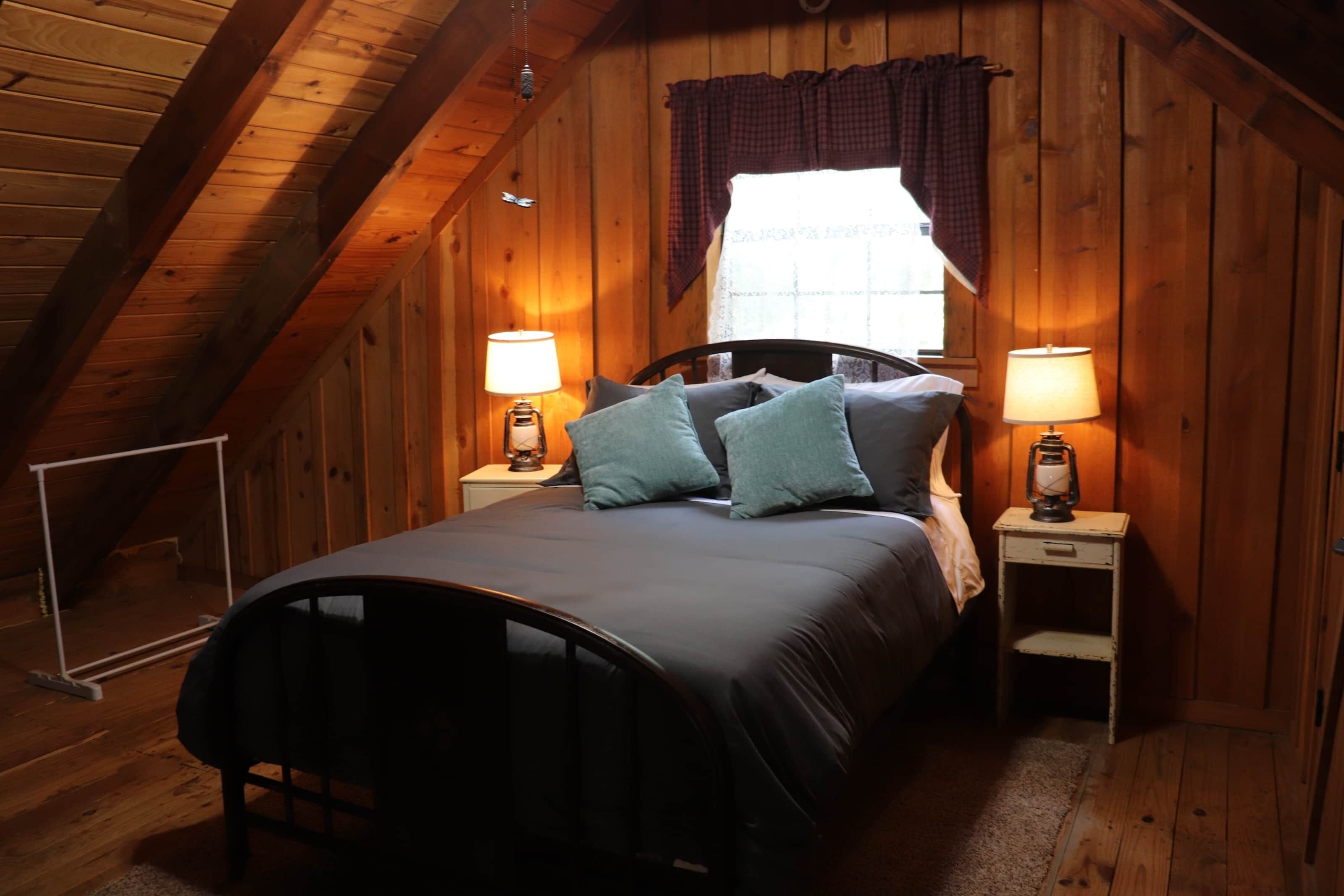 Une chambre mansardée chaleureuse, avec un lit, deux tables de chevet et une fenêtre avec des rideaux.