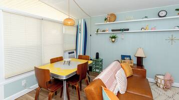 Ein kleiner Wohnraum mit Esstisch, Stühlen, einer Couch und einem Surfbrett.