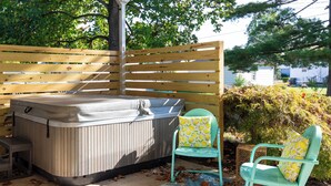 A hot tub with a wooden fence backdrop, a chair with a lemon pattern cushion, and a blue patterned rug on the ground. - Mid-Century Modern Themed Surf House (Vermilion)