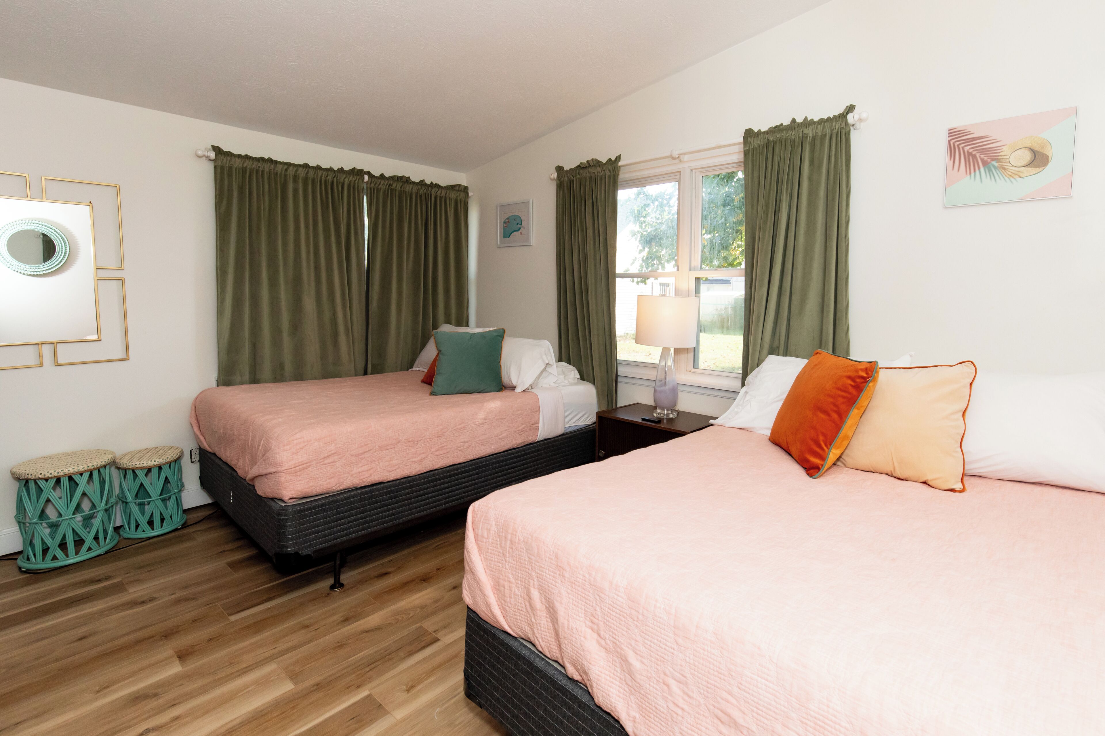Habitación de hotel con dos camas individuales, piso de madera, ventana con cortinas, una lámpara y un cuadro en la pared.