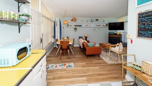 A compact living space with a dining area, a sofa, and a kitchen area with a microwave. - Mid-Century Modern Themed Surf House (Vermilion)