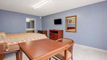 Quarto de hotel com cama, mesa de madeira, cadeira, cômoda, televisão e espelho.