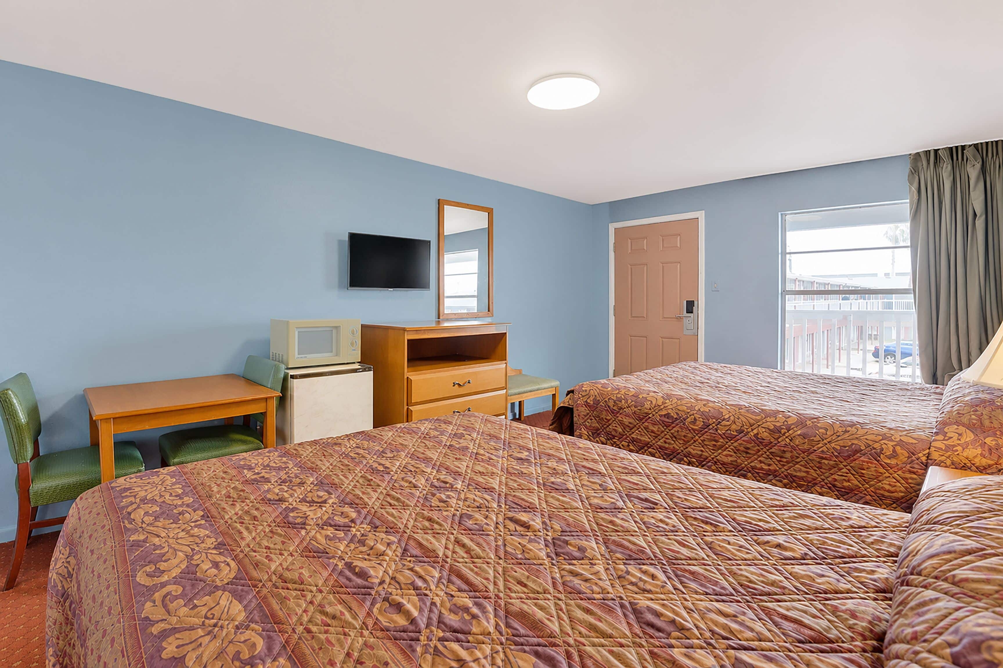 A hotel room with two beds, a desk, a television, and a window with curtains.