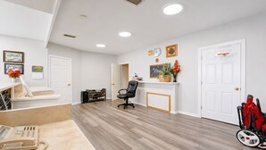 A spacious room with a wooden floor, a desk with a telephone, a chair, a shoe rack, and a door with a basketball hoop. - Valley Motel Corpus Christi Near Airport I 37 (Corpus Christi)