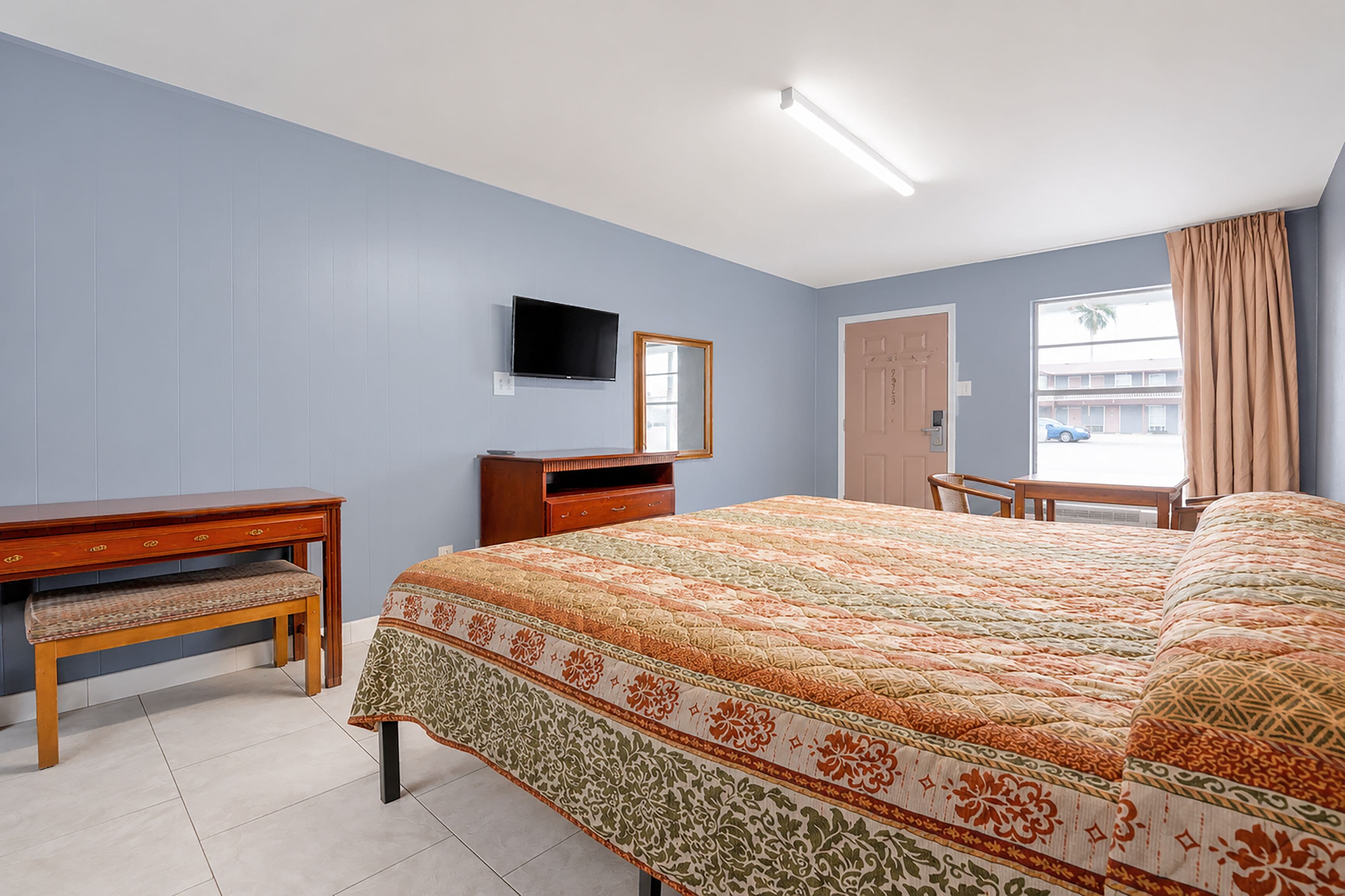 A hotel room with a bed, a desk, a television, a mirror, and a window with curtains.