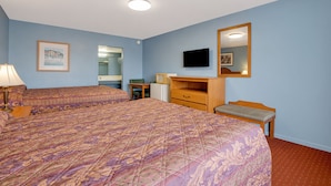A hotel room with two beds, a desk, a chair, a dresser, a television, and a mirror.