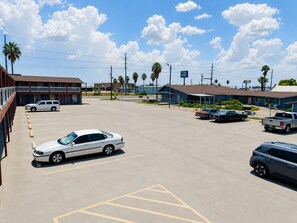A parking lot with several cars, a building with a red facade, and a clear blue sky with clouds.