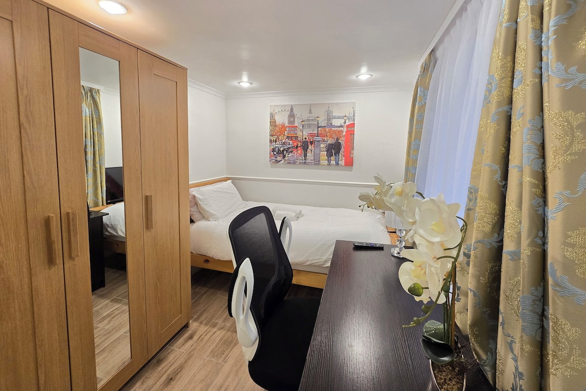 Ein Schlafzimmer mit Bett, Schreibtisch, Stuhl, Kleiderschrank, einem Gemälde und einem Vorhang.