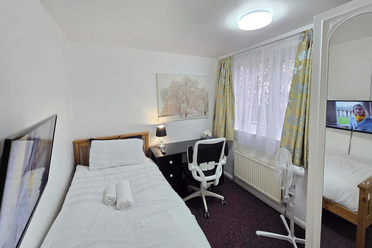 Ein Hotelzimmer mit Bett, Schreibtisch, Stuhl, Fernseher und einem Fenster mit Vorhängen.
