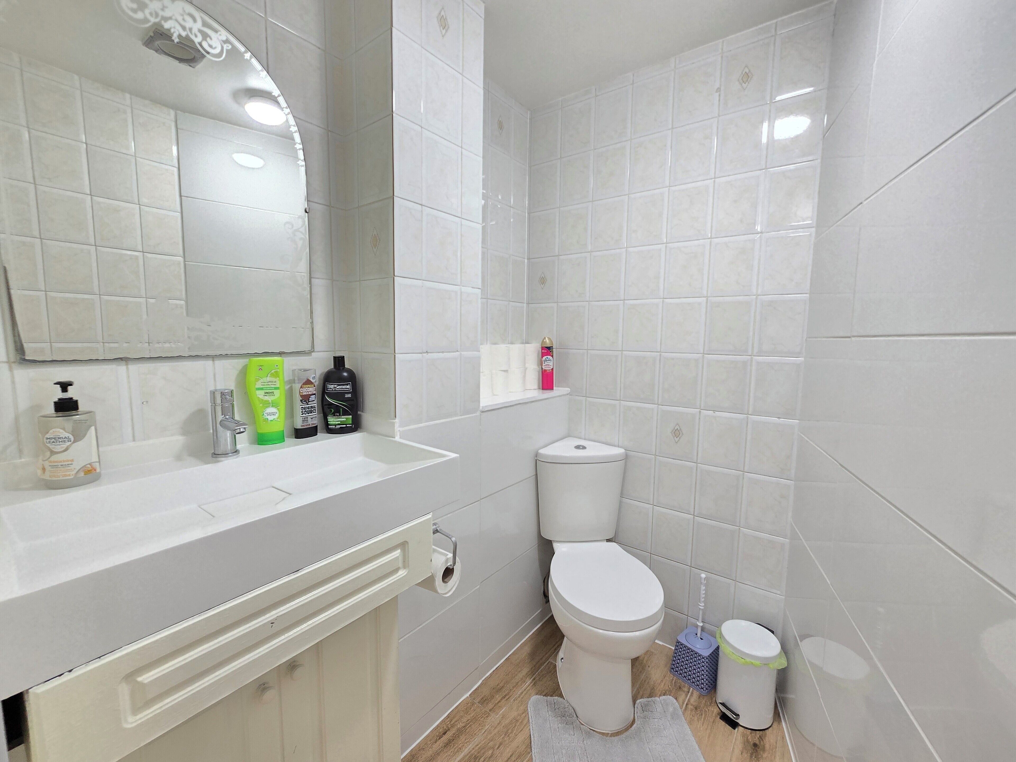 A bathroom with white tiles, a sink, a toilet, and a mirror.