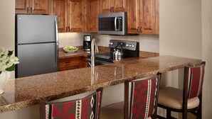 Una cocina con gabinetes de madera, un refrigerador de acero inoxidable, un microondas, una estufa y un fregadero.