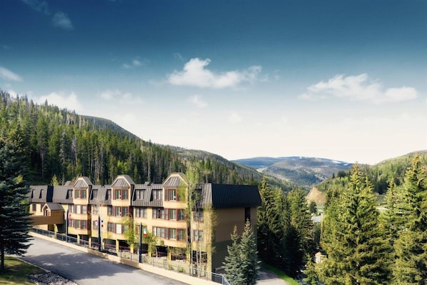 A multi-story hotel with a symmetrical facade, set in a mountainous area with dense forest. - West Vail 1 Bedroom Condo at Streamside (Vail)