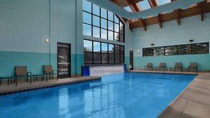 Una piscina interior con paredes de vidrio transparente, suelo de baldosas y techo de madera.