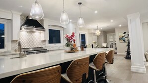 Una cocina moderna con una isla grande, taburetes de bar, iluminación colgante y una campana extractora de acero inoxidable.
