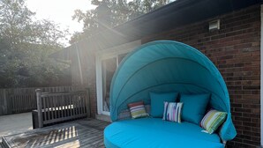 Una cama colgante redonda de mimbre con dosel color turquesa y cojines de colores sobre una terraza de madera.